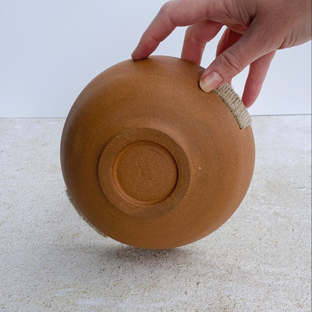 Hand holding a ceramic bowl on a textured surface with a light background