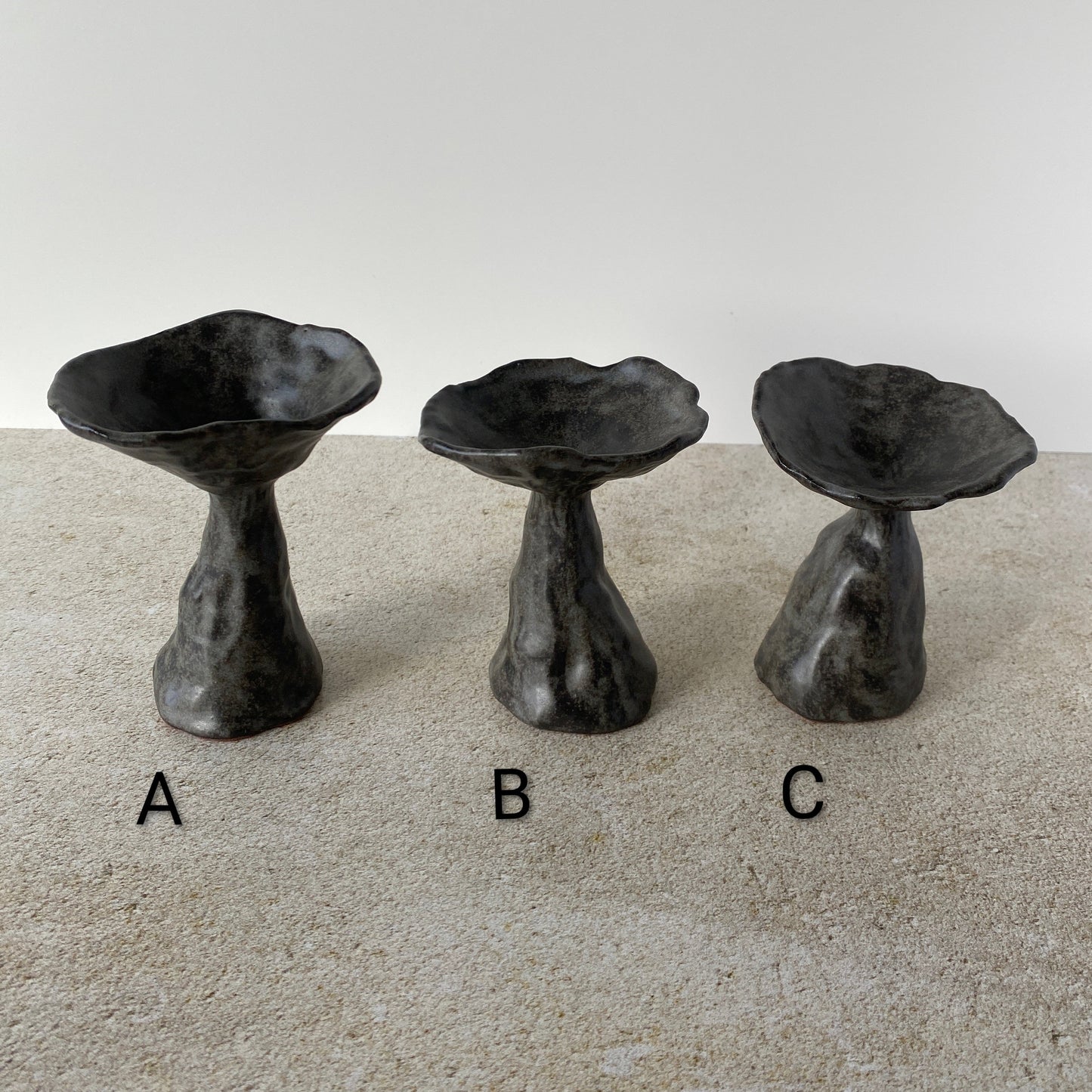 Three black ceramic mushrooms labeled A, B, and C on a beige surface with a white background