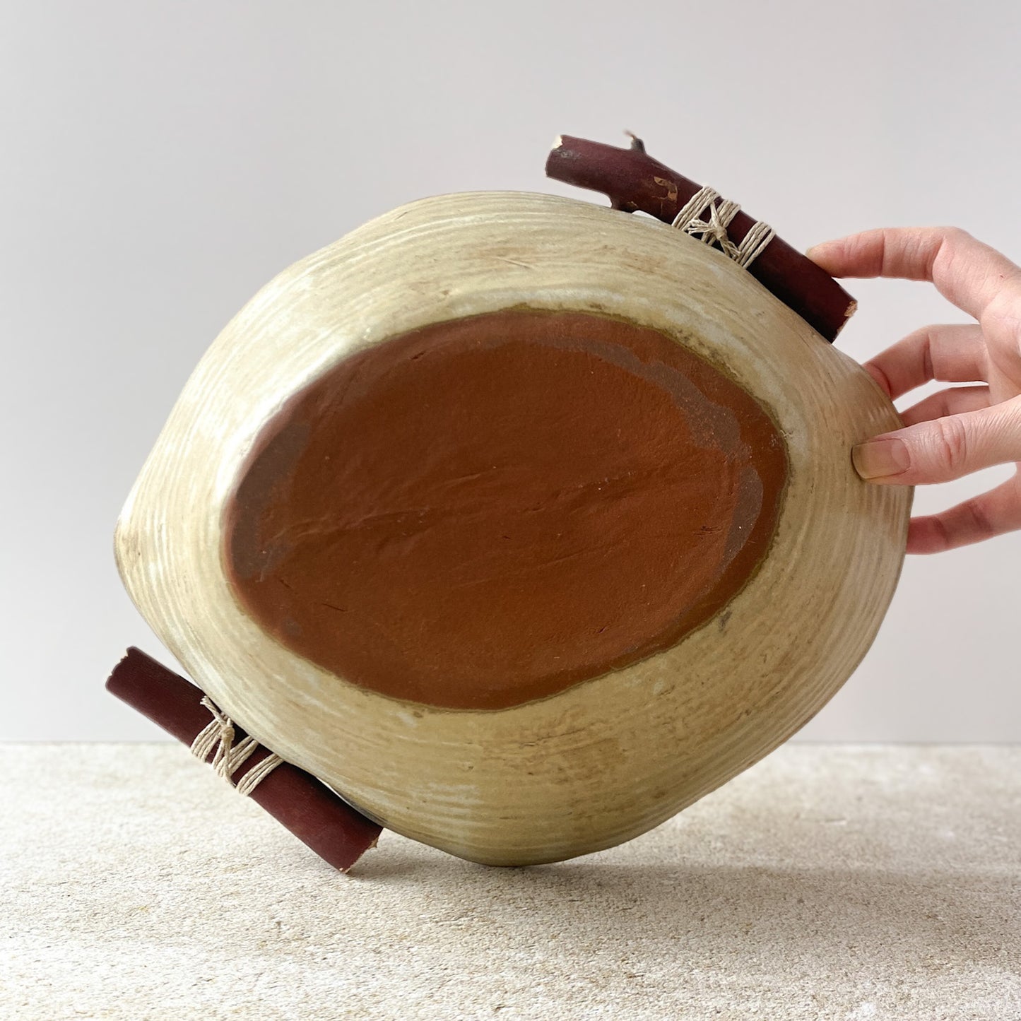 Hand displaying the bottom of a ceramic bowl on a light surface.