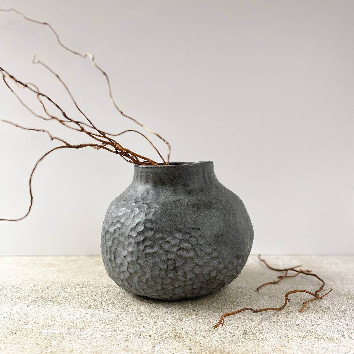 Textured gray vase with branches on a light surface and white background