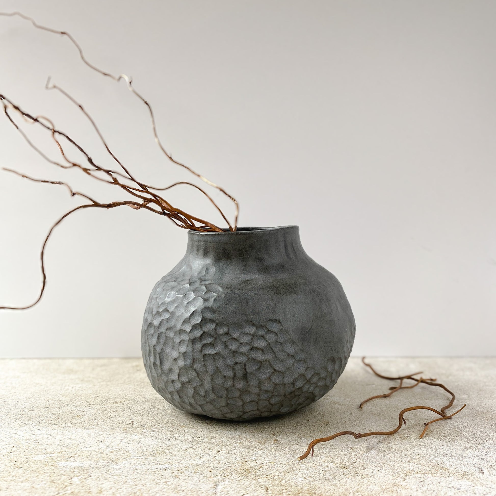 Textured gray vase with branches on a light surface and white background