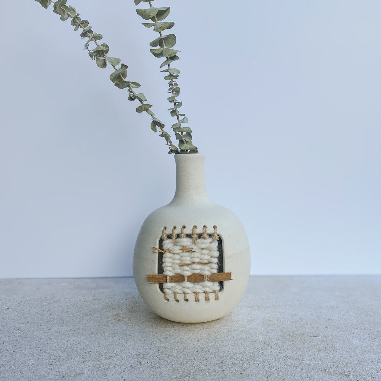 White vase with small weaving on a plain background