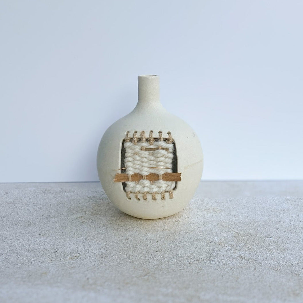 White ceramic vase with small weaving on a light surface