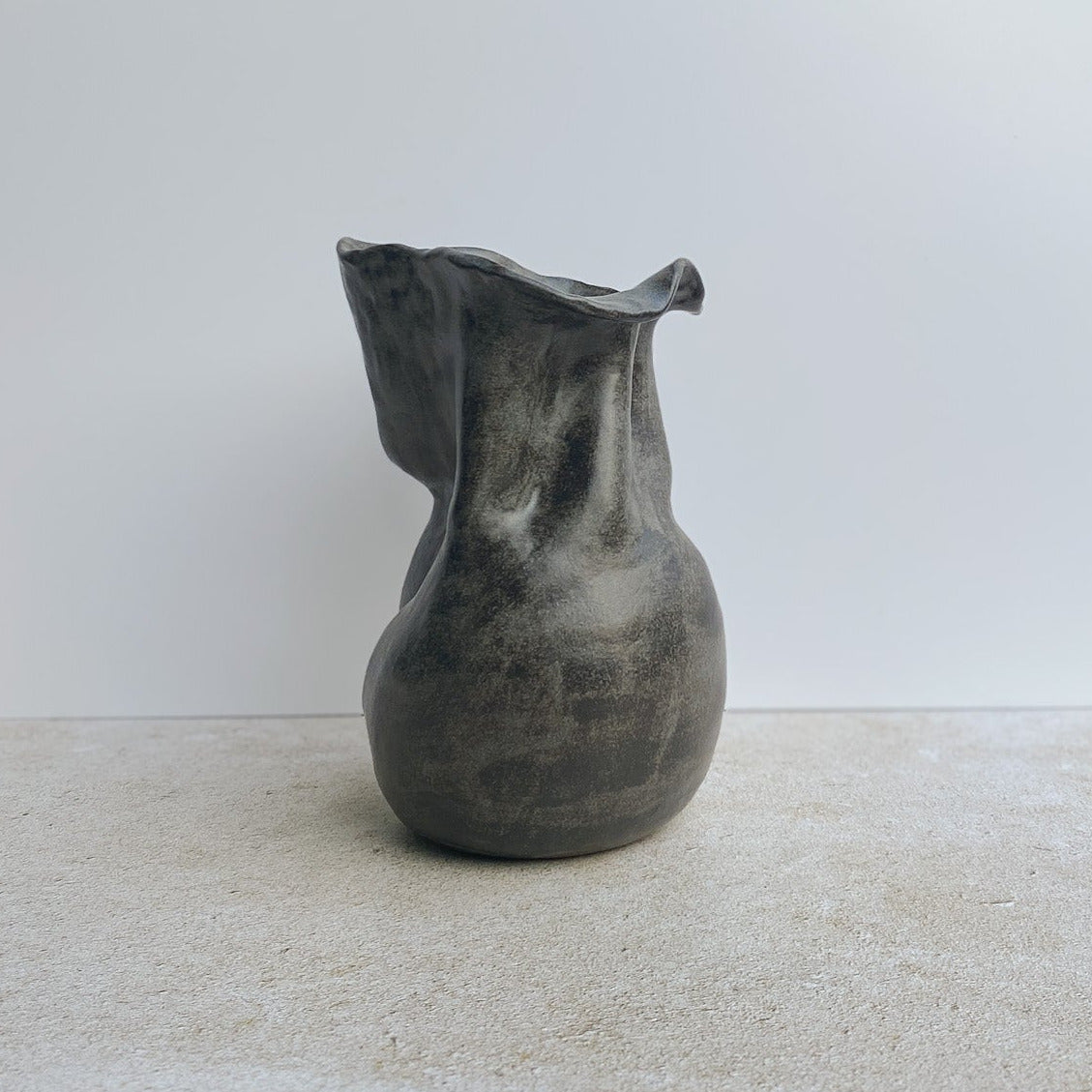 Gray ceramic sculpture vase on a light-colored floor with a white wall in the background