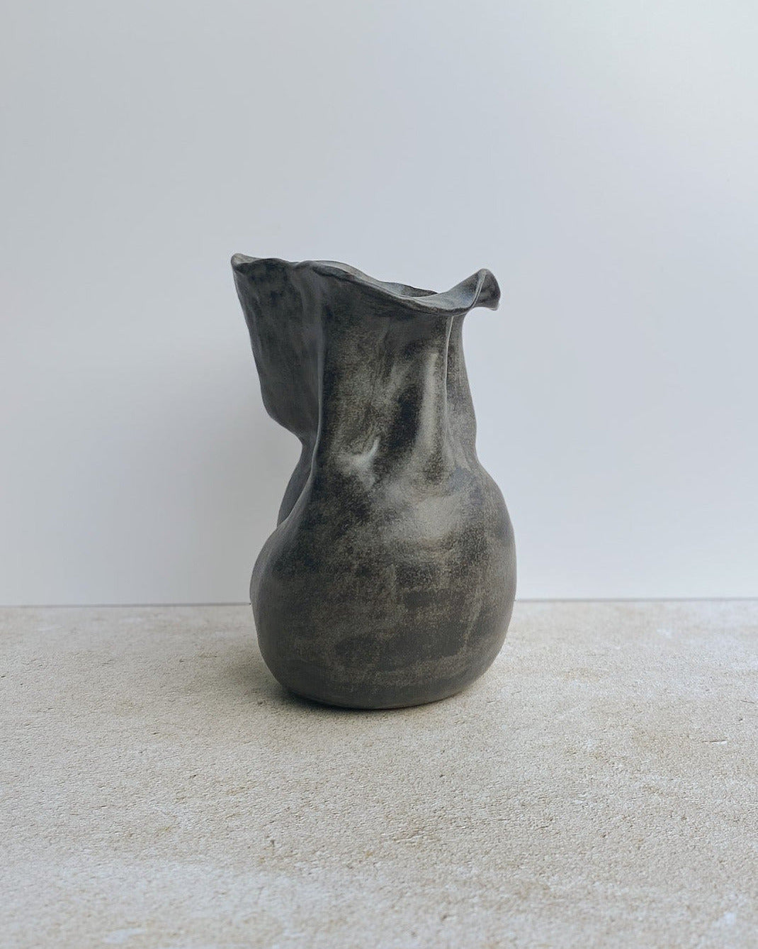 Gray ceramic vase on a light-colored floor with a white wall in the background