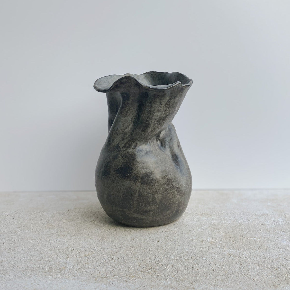 Gray ceramic sculpture vase on a white surface with a neutral background