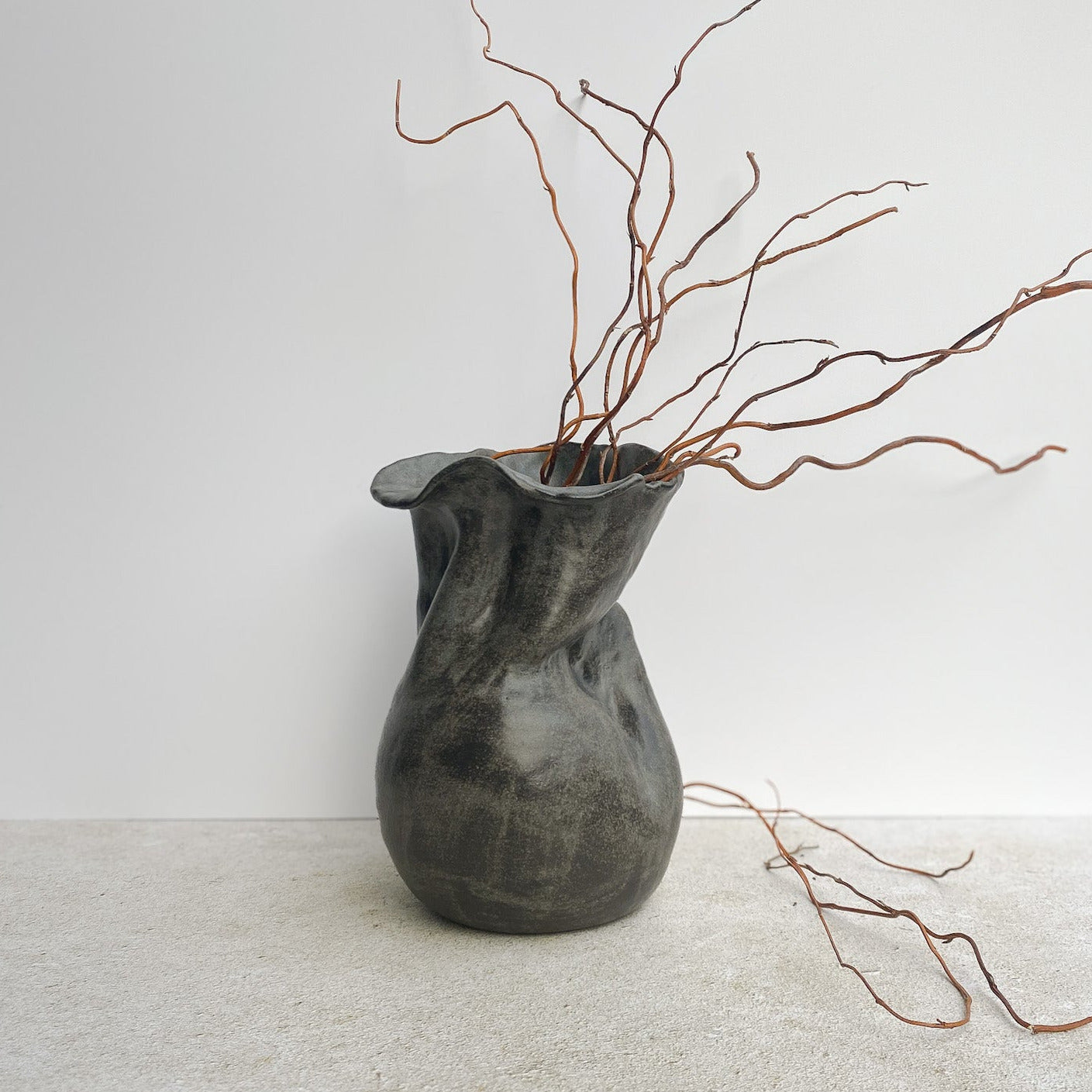 Dark gray ceramic sculpture vase with branches on a light gray surface