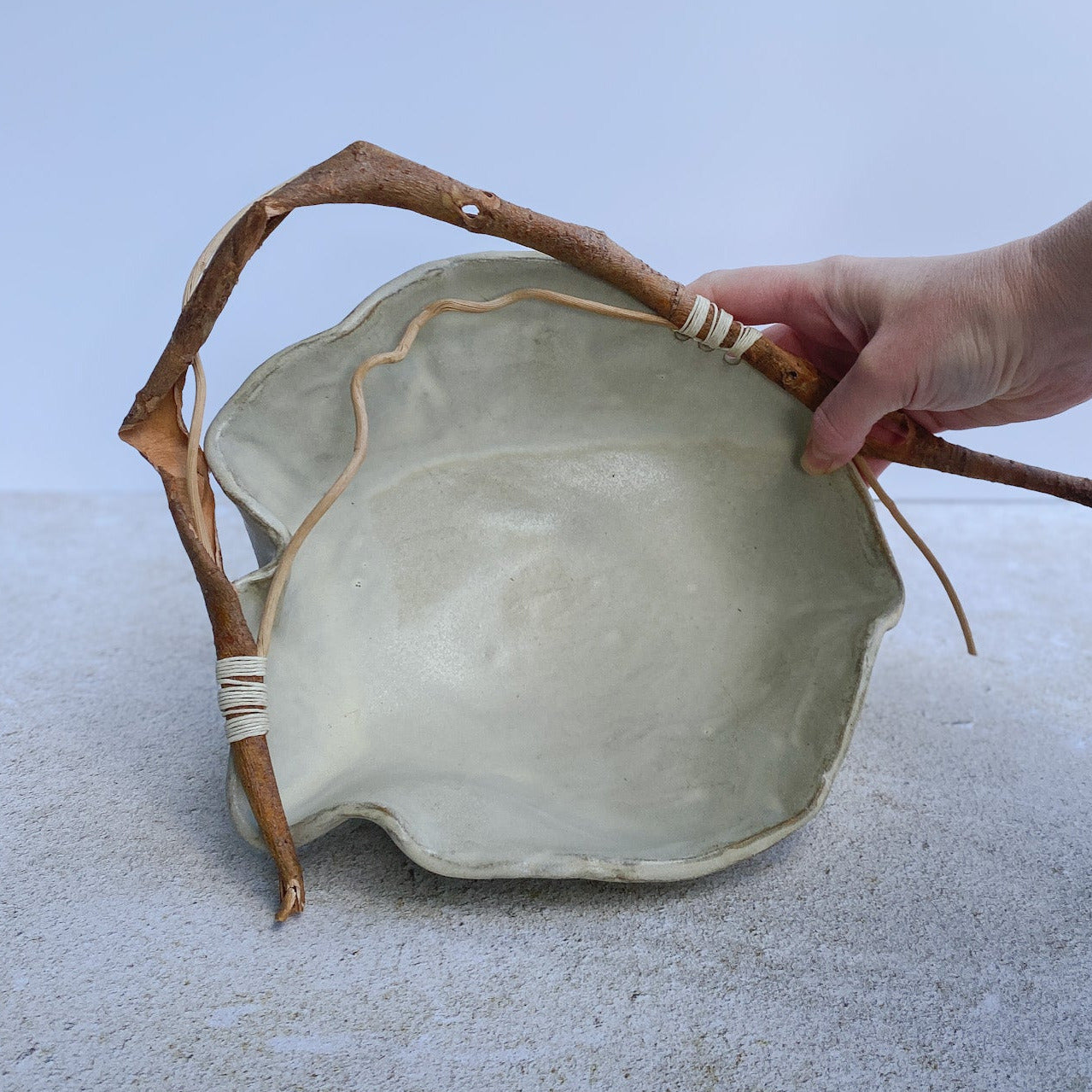 Hand holding a ceramic bowl with natural elements on a light background