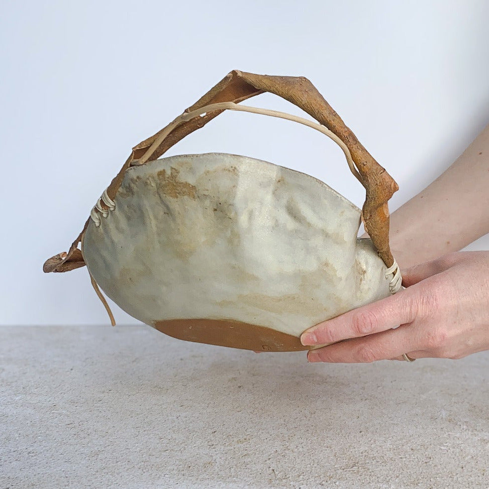 Ceramic bowl with wooden handle held by a person on a textured surface