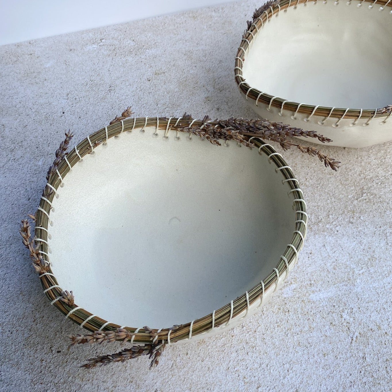 Two white ceramic bowls with dried lavender rims on a textured surface