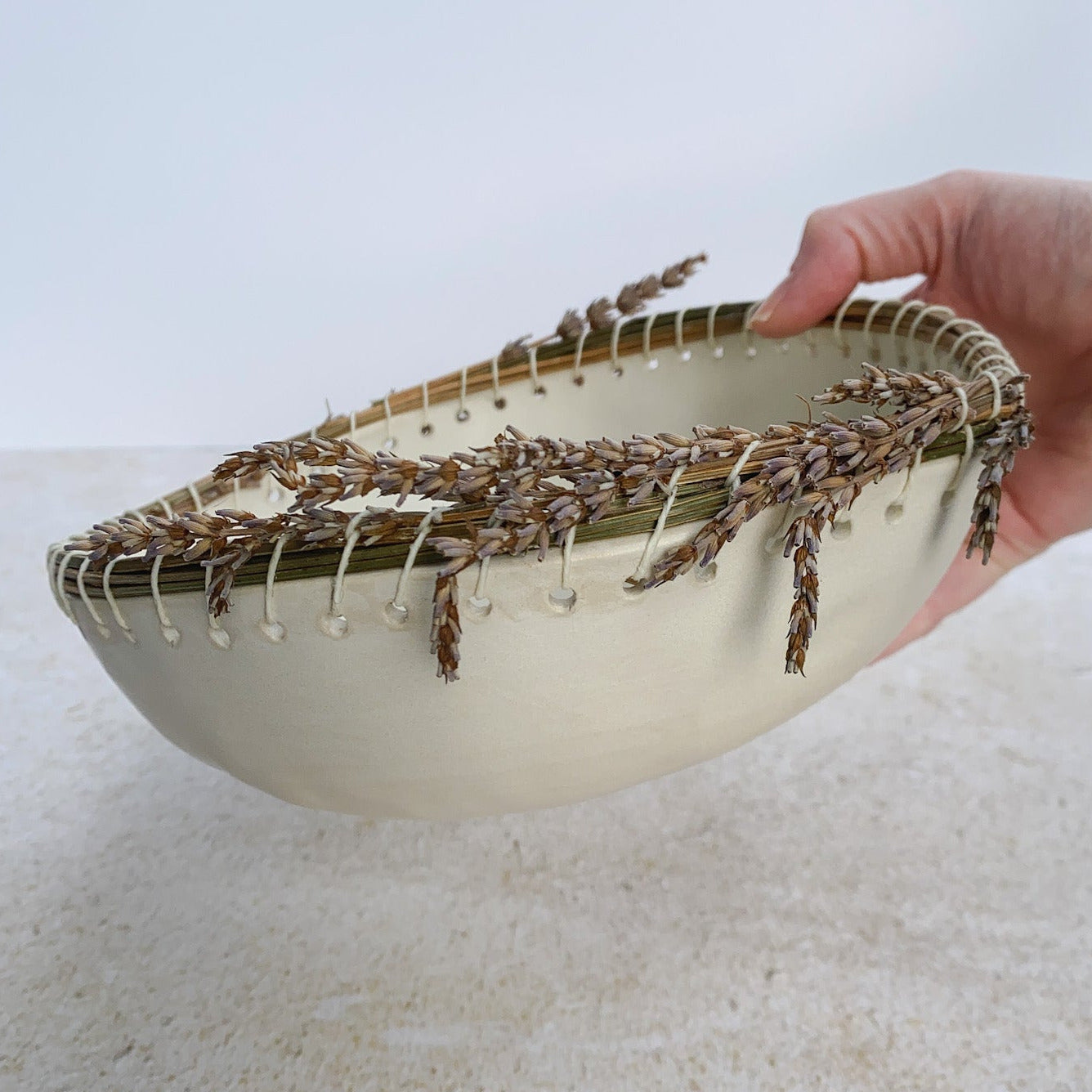 Hand holding a ceramic bowl with dried lavender on a light background