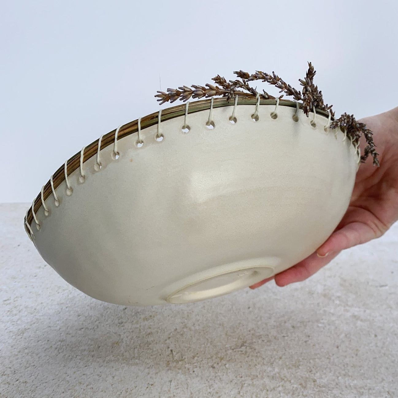Hand holding a white ceramic bowl with dried lavender over a light-colored surface
