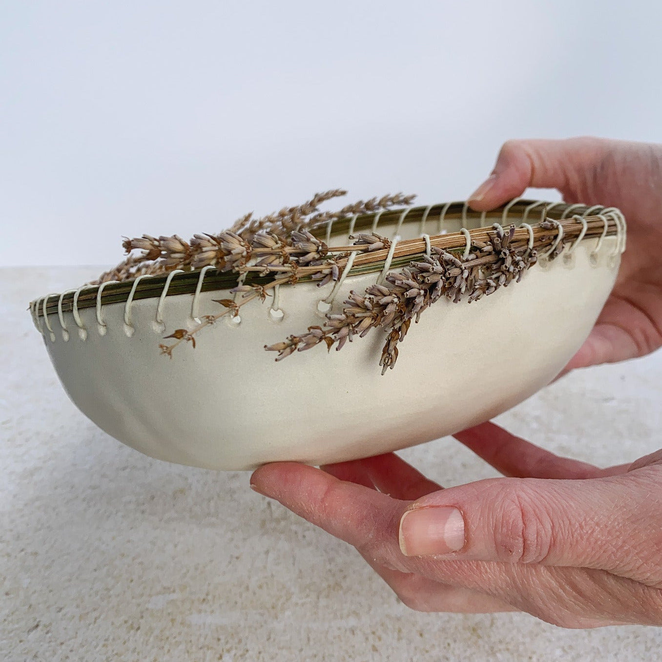 Hand holding a white ceramic bowl with dried lavender on a light background
