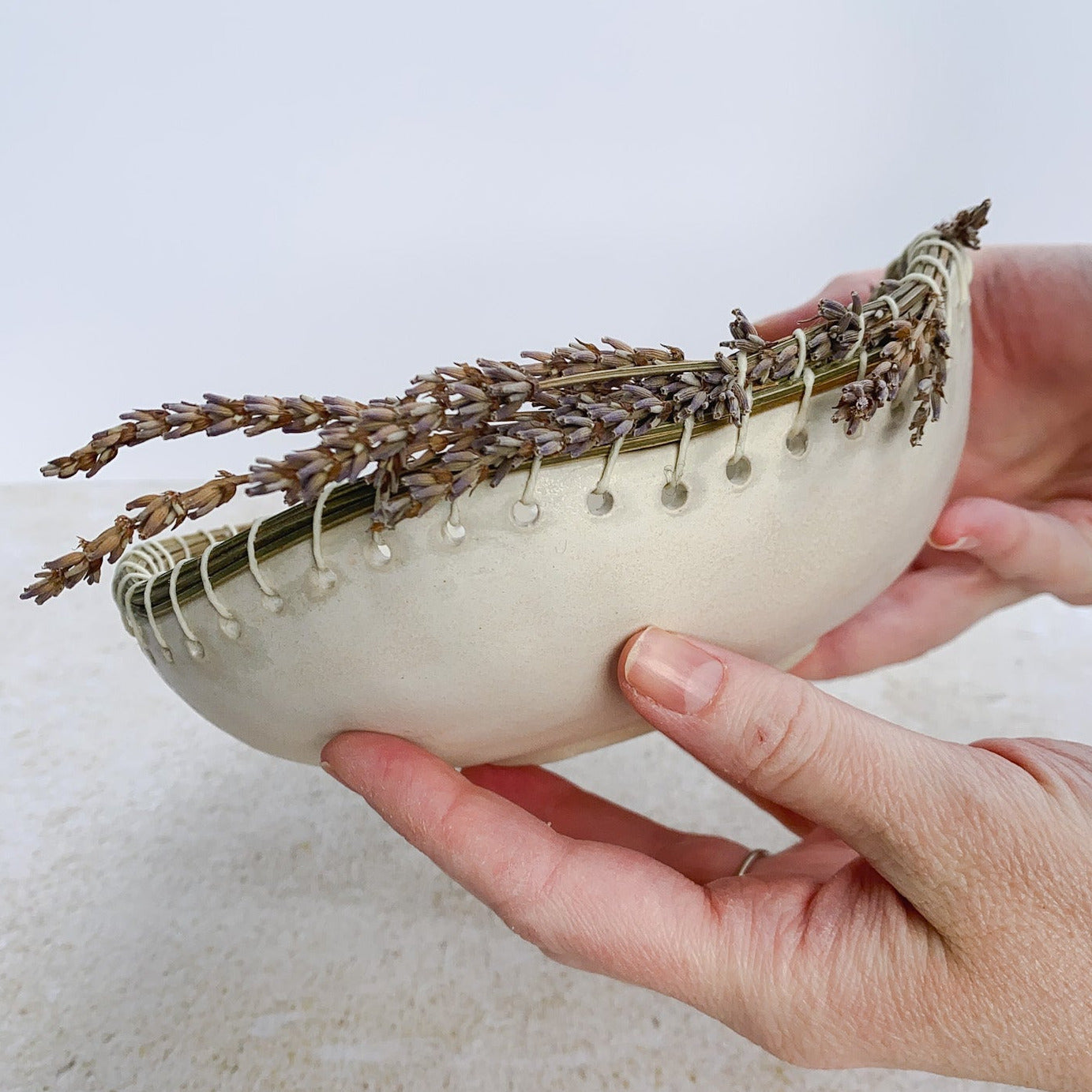 Hand holding a white ceramic bowl with dried lavender on a light background