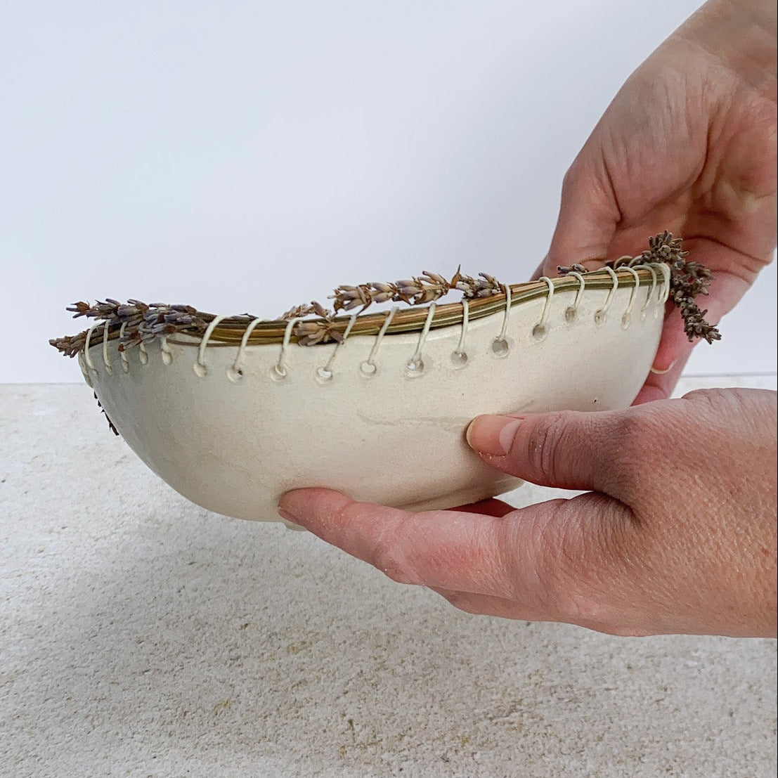 Hand holding a small ceramic bowl with dried lavender stalks on a textured surface