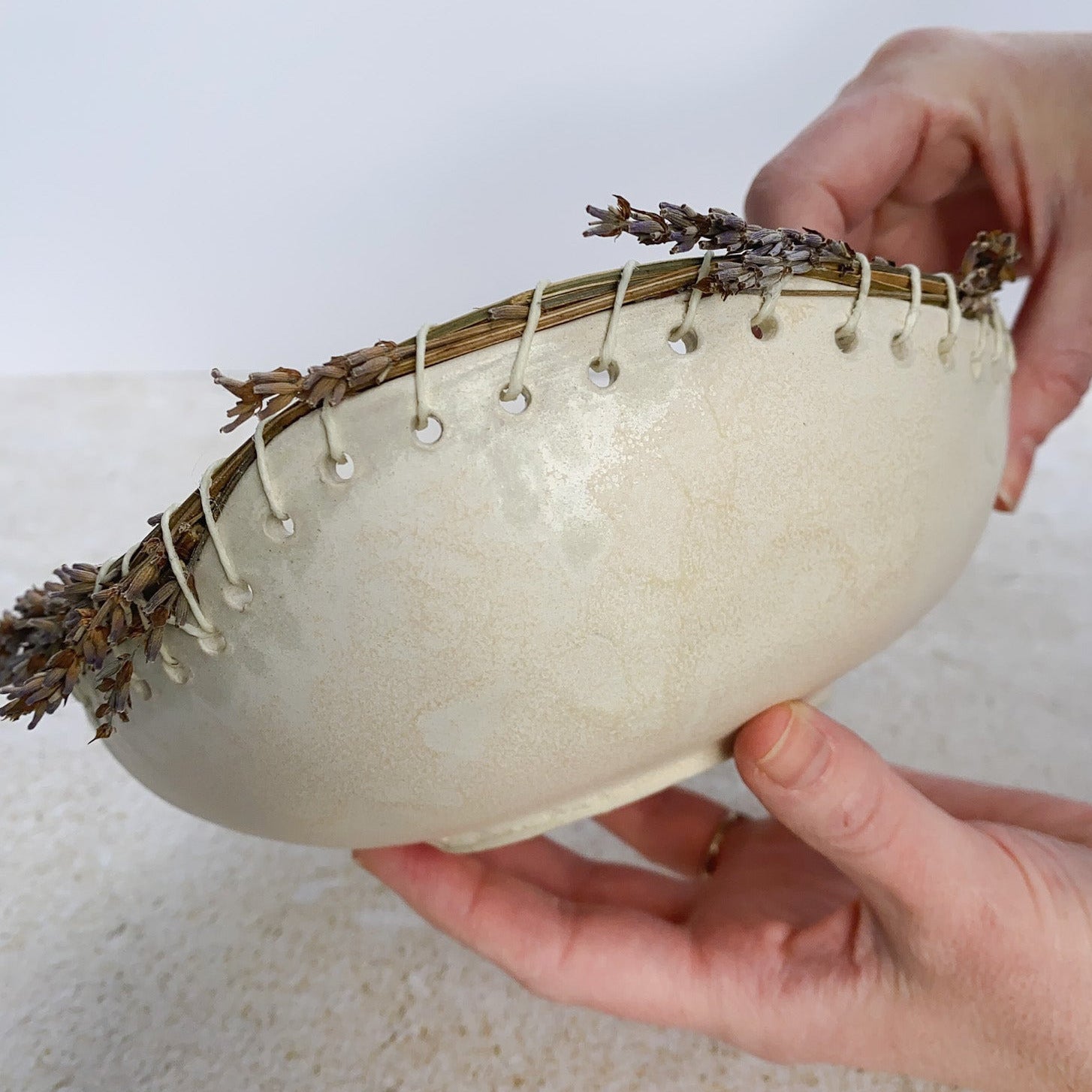 Person holding a white bowl with lavender and string on a light background