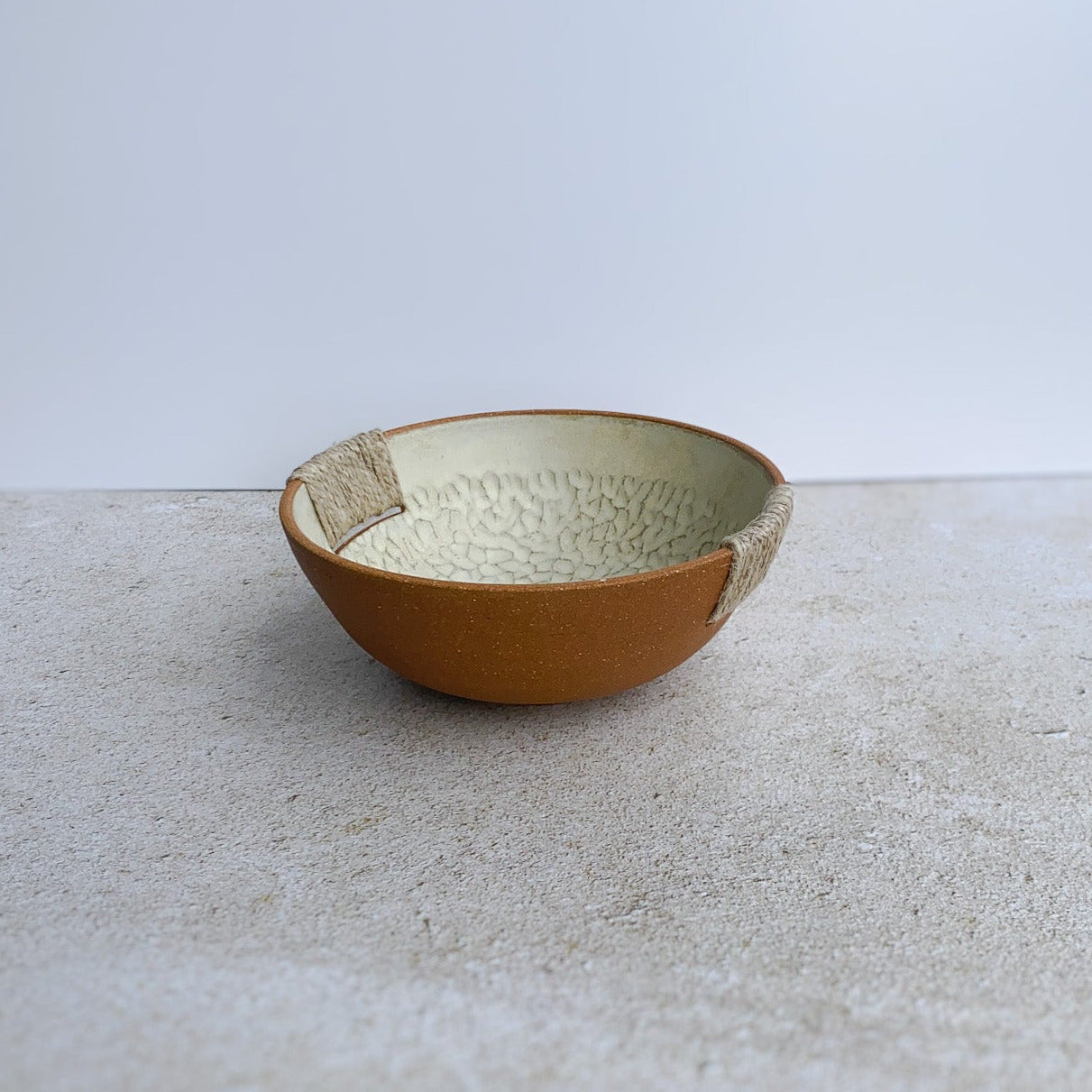 Ceramic bowl with textured surface and twine accents on a light gray background