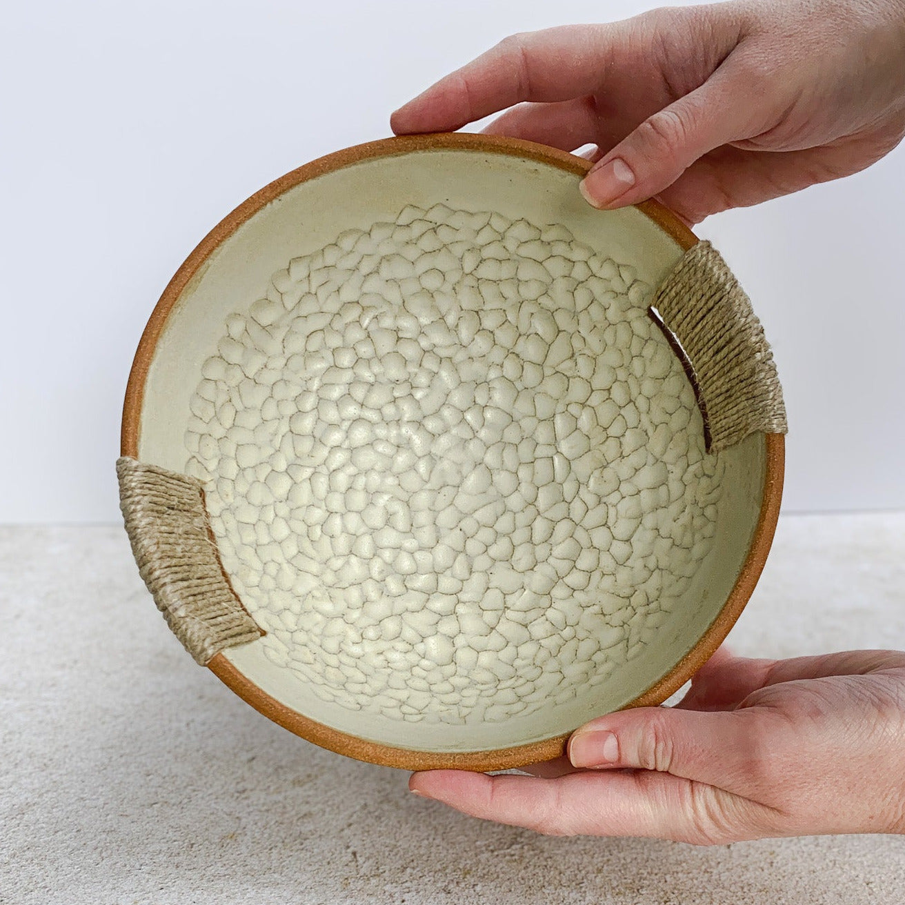 Ceramic bowl with textured surface held by a hand on a light background