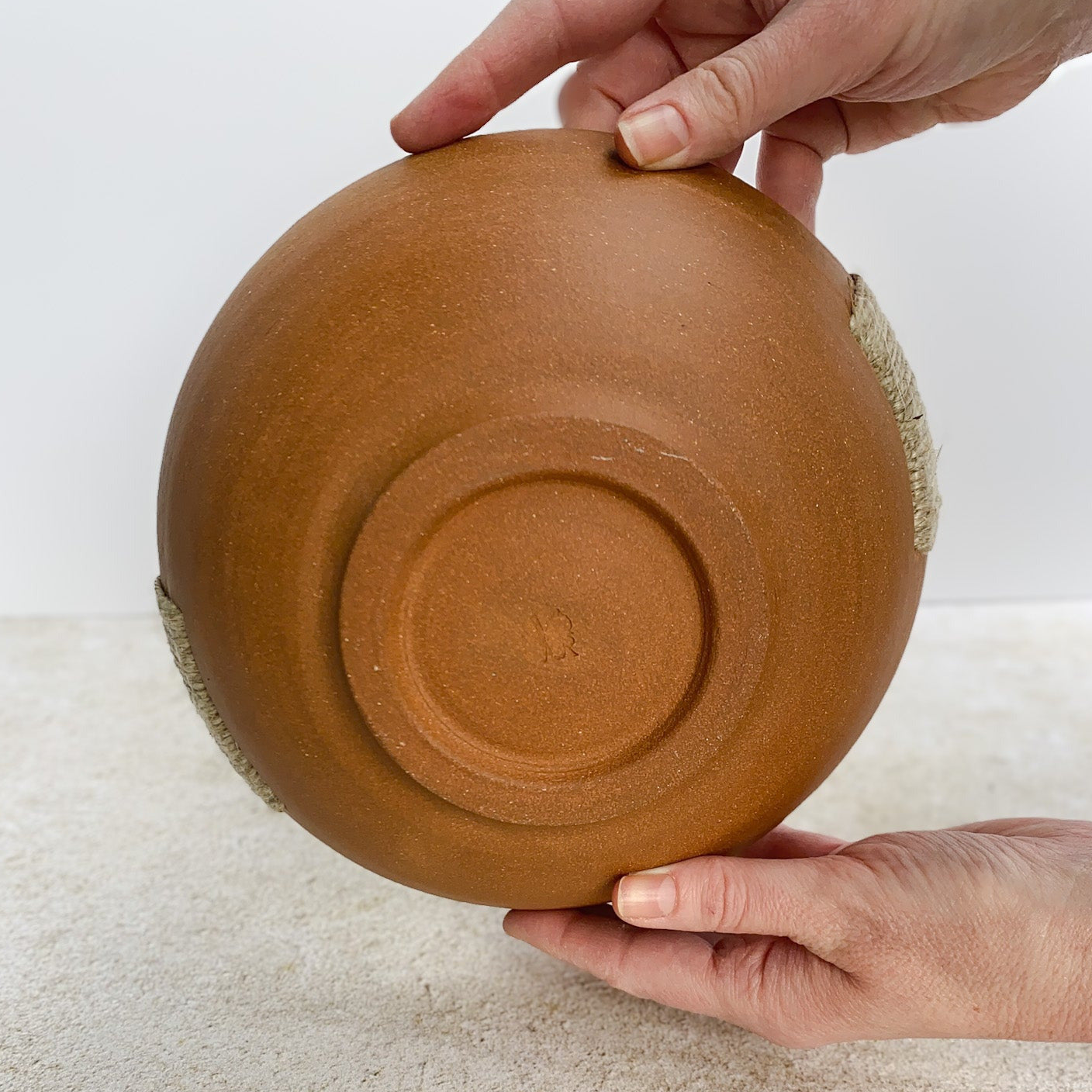 Person holding an unglazed ceramic bowl on a light surface