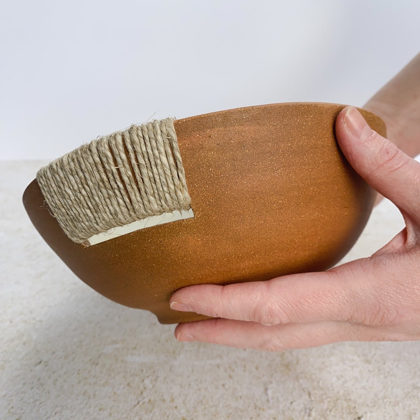 Hand holding a ceramic bowl with a twine accent on a light background