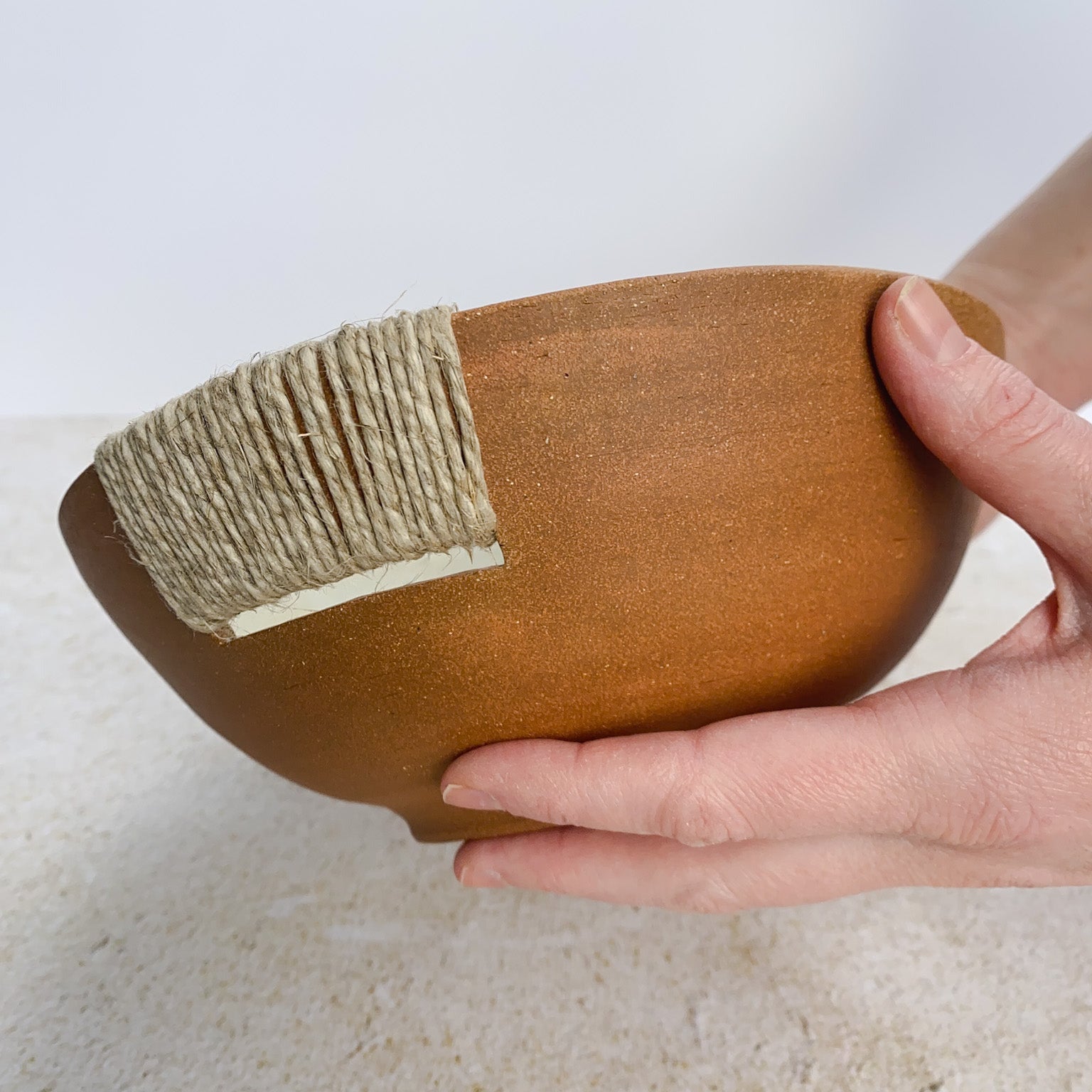 Hand holding a ceramic bowl with a twine accent on a light background