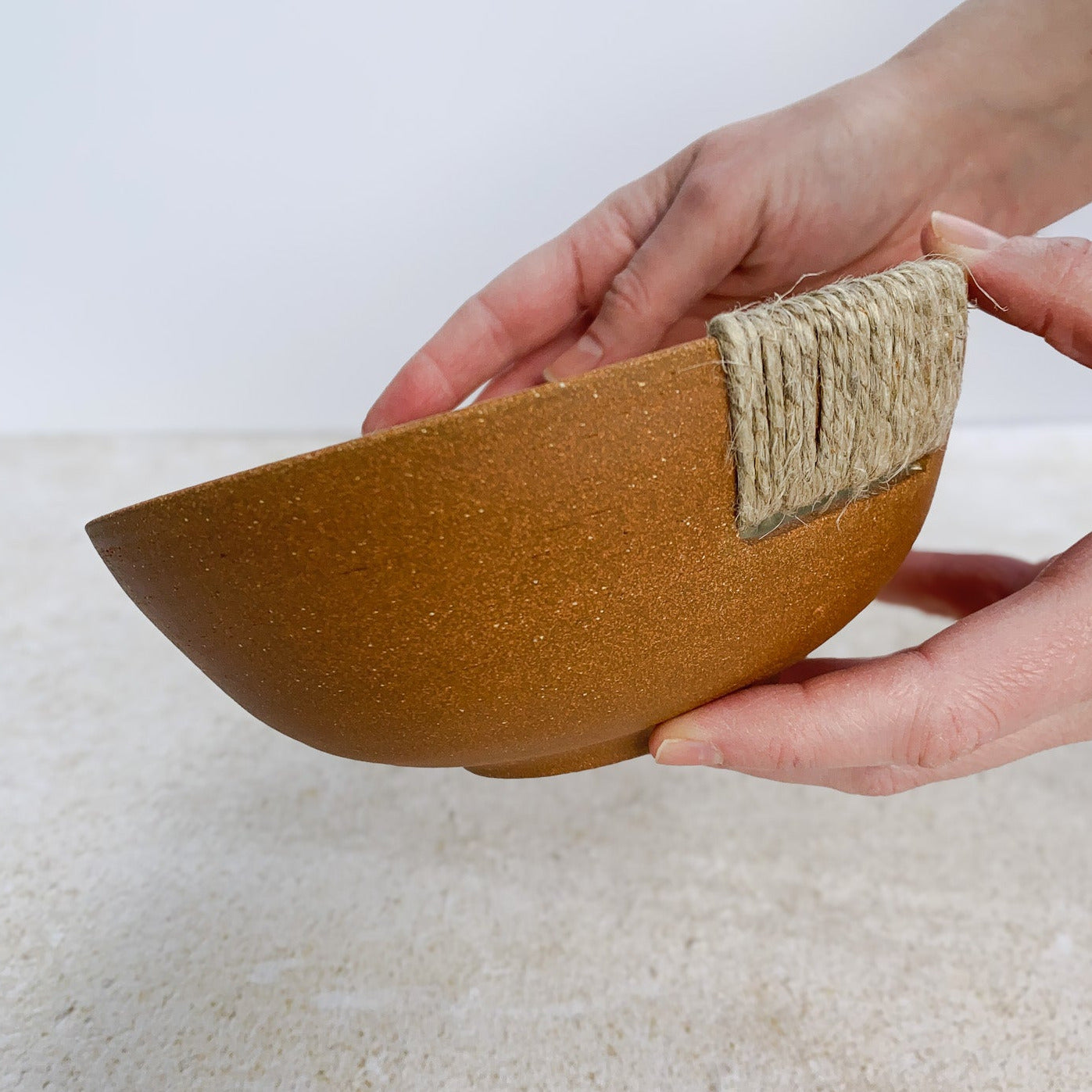 Person holding an unglazed ceramic bowl with hemp twine on a light surface