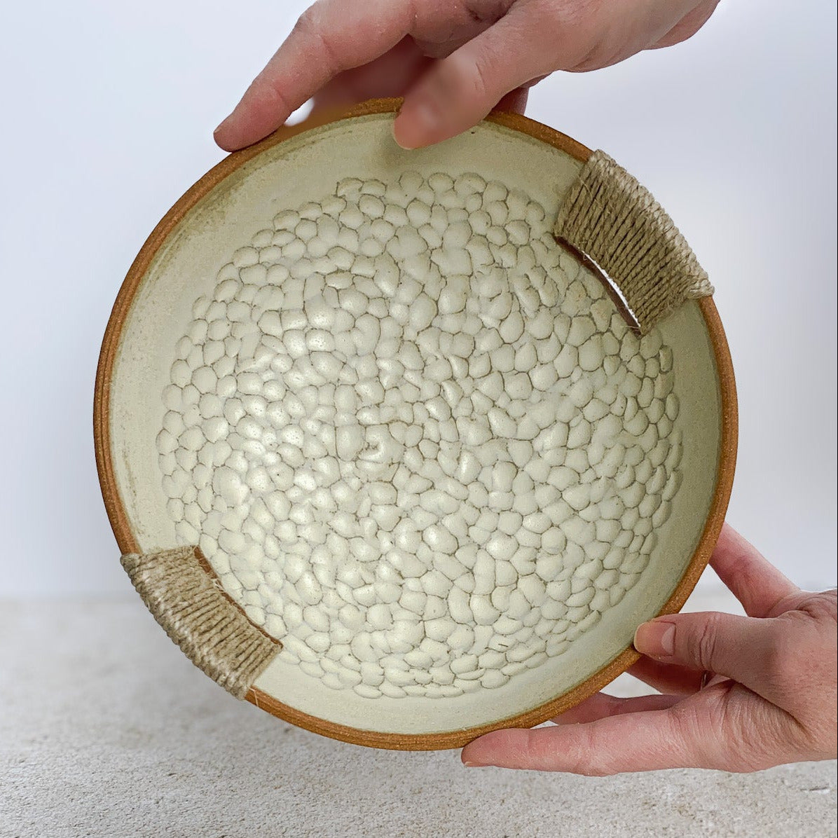 Ceramic bowl with textured surface held by a hand on a light background