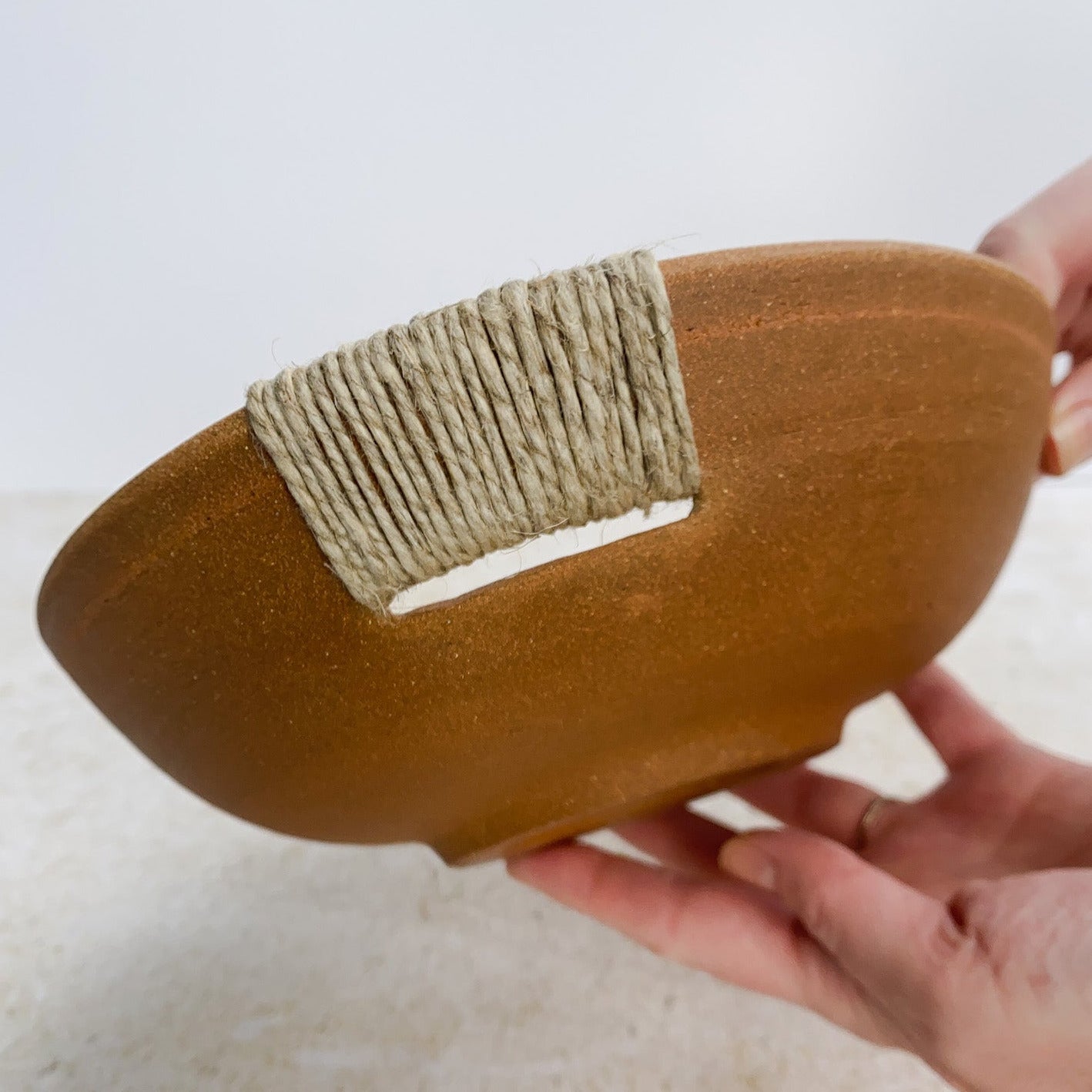 Unglazed ceramic bowl with hemp twine handle held by a hand on a light background