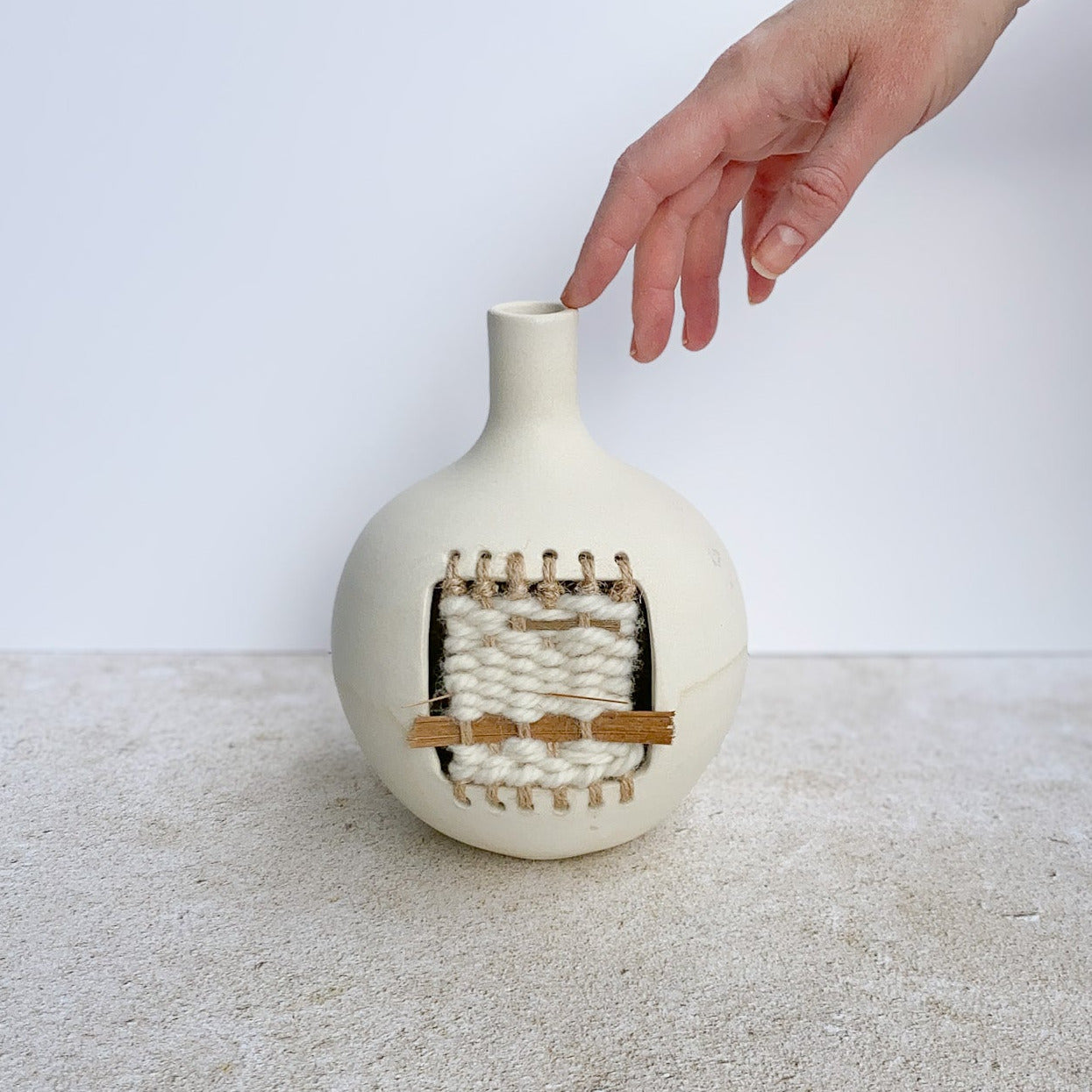 Ceramic vase with woven design on a textured surface