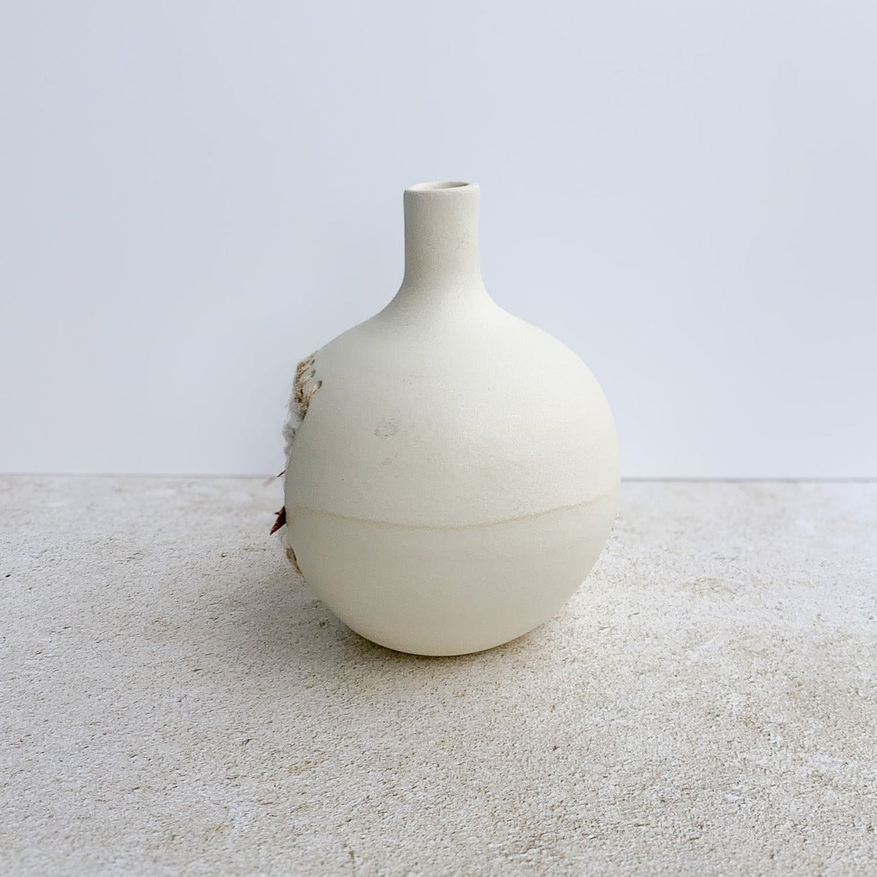 White ceramic vase on a textured surface with a light gray background
