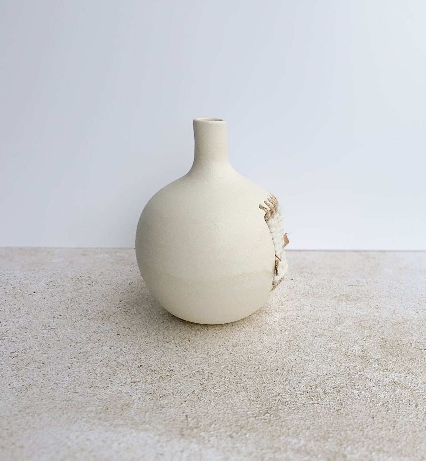 White ceramic vase on a textured surface with a light gray background