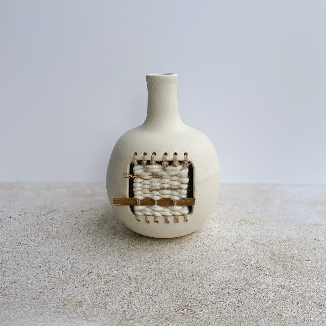 White ceramic vase with woven design on a textured surface