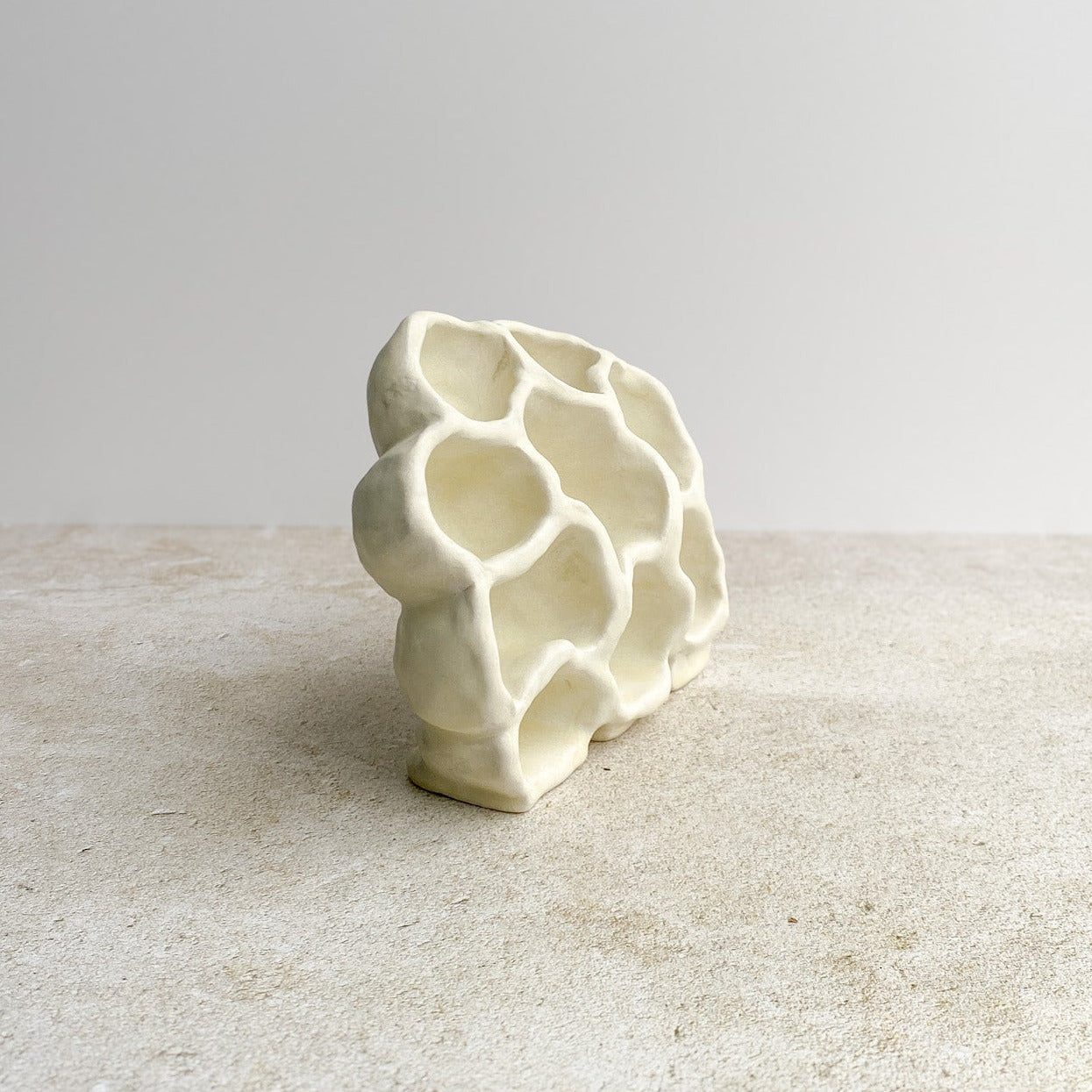 White ceramic honeycomb sculpture on a textured surface with a light gray background