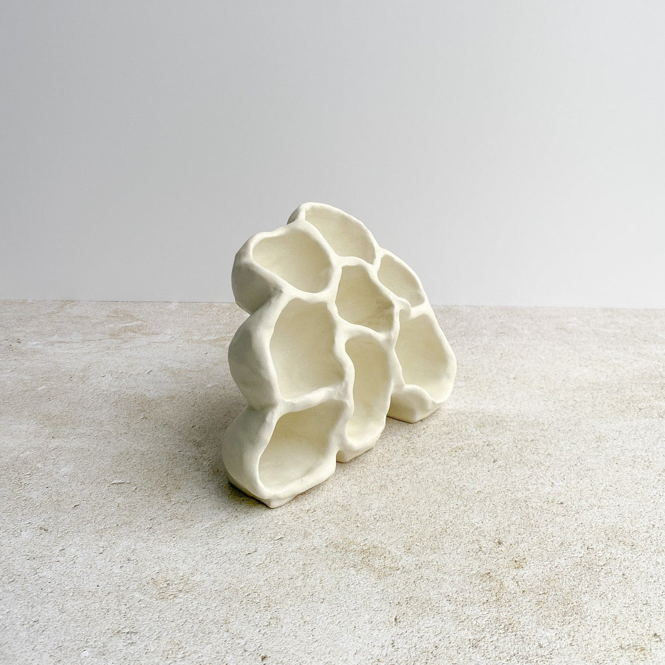 White ceramic sculpture on a textured surface with a light gray background
