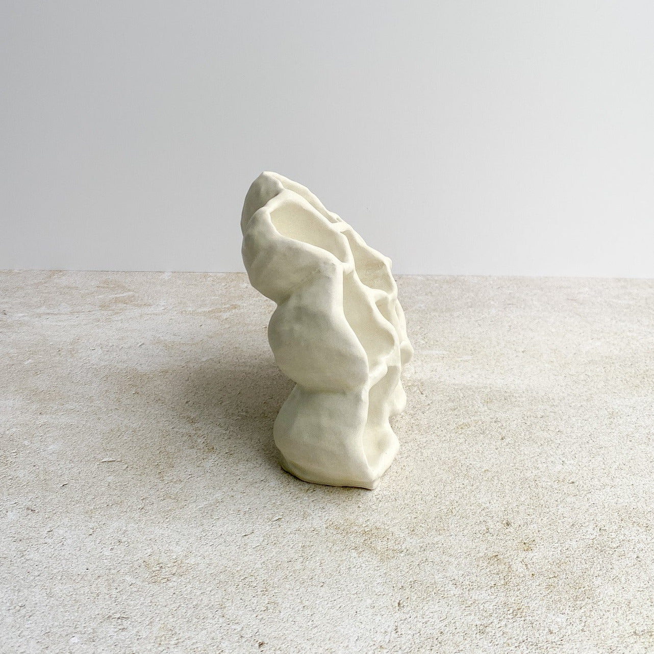 White ceramic sculpture on a textured surface with a light gray background