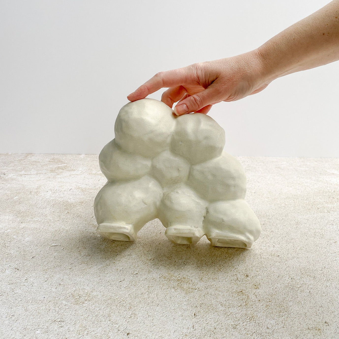 White cloud-shaped ceramic object being held by a hand on a light background