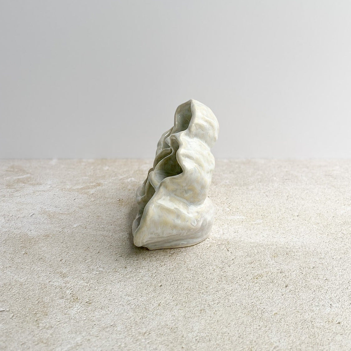 Ceramic sculpture with an organic form on a textured surface with a light gray background