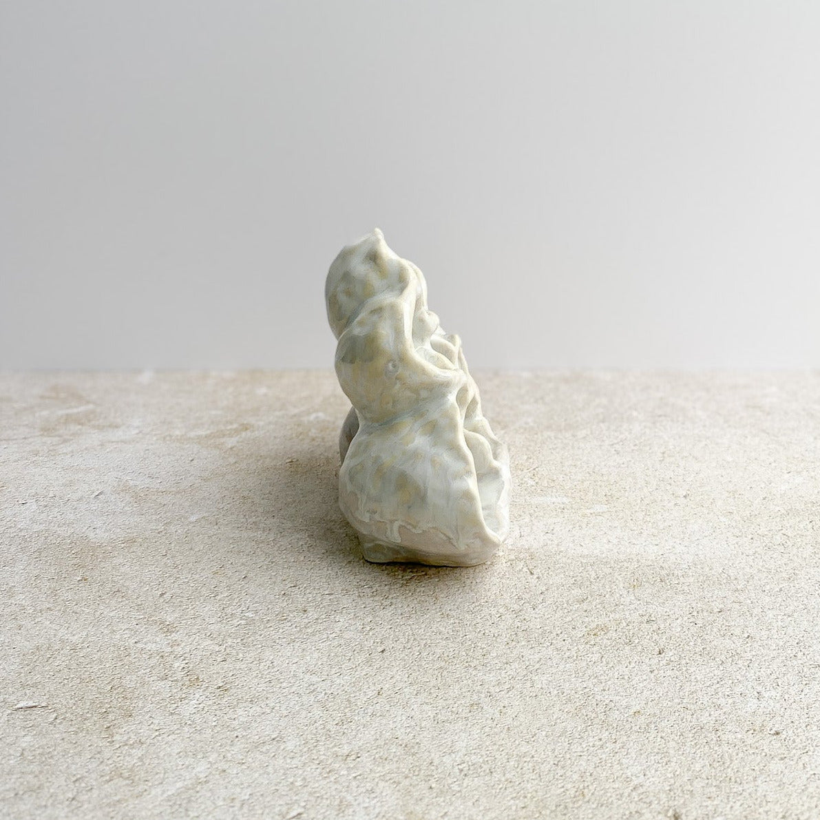 Small white ceramic sculpture on a textured surface with a light gray background