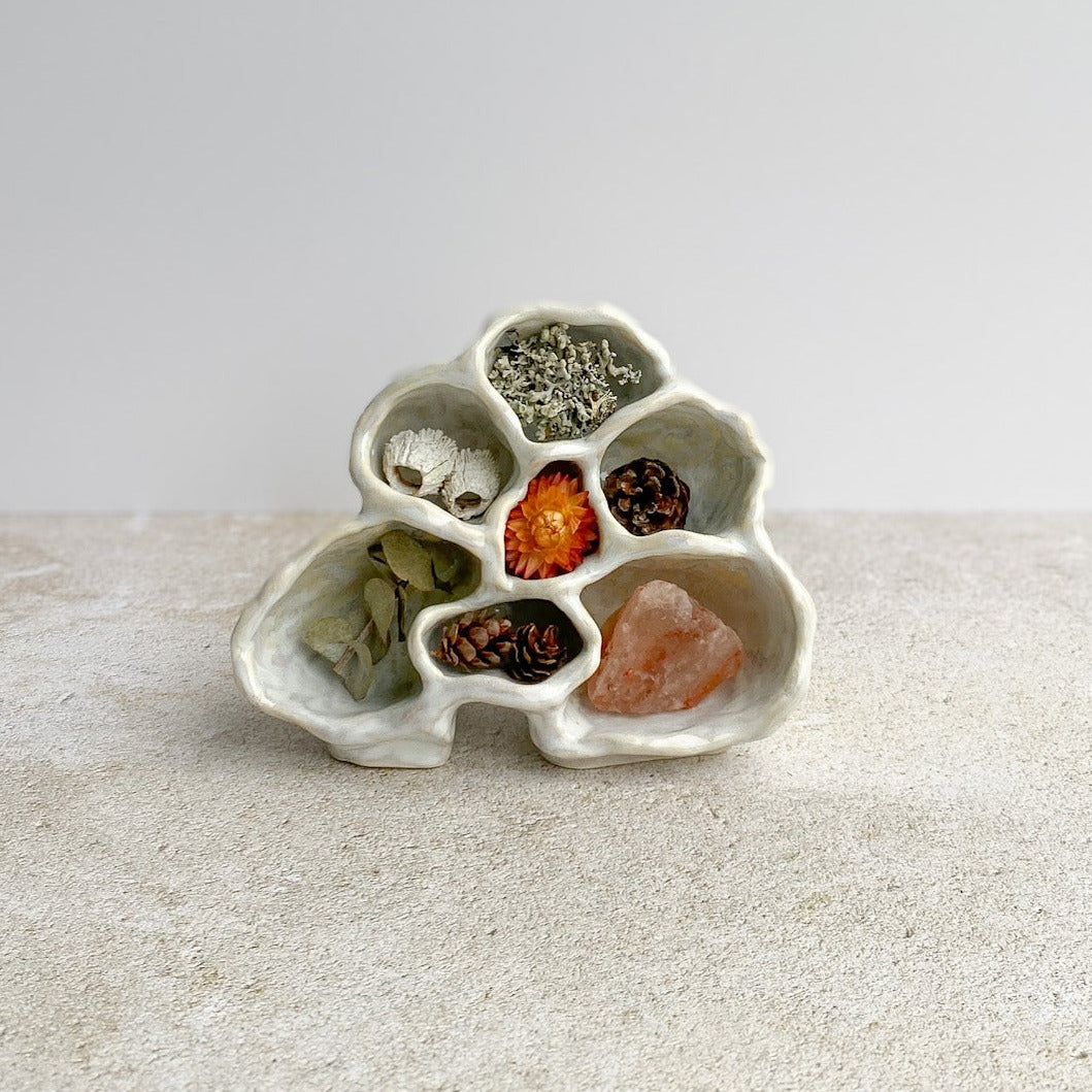 Small ceramic sculpture holder with colorful stones on a textured surface