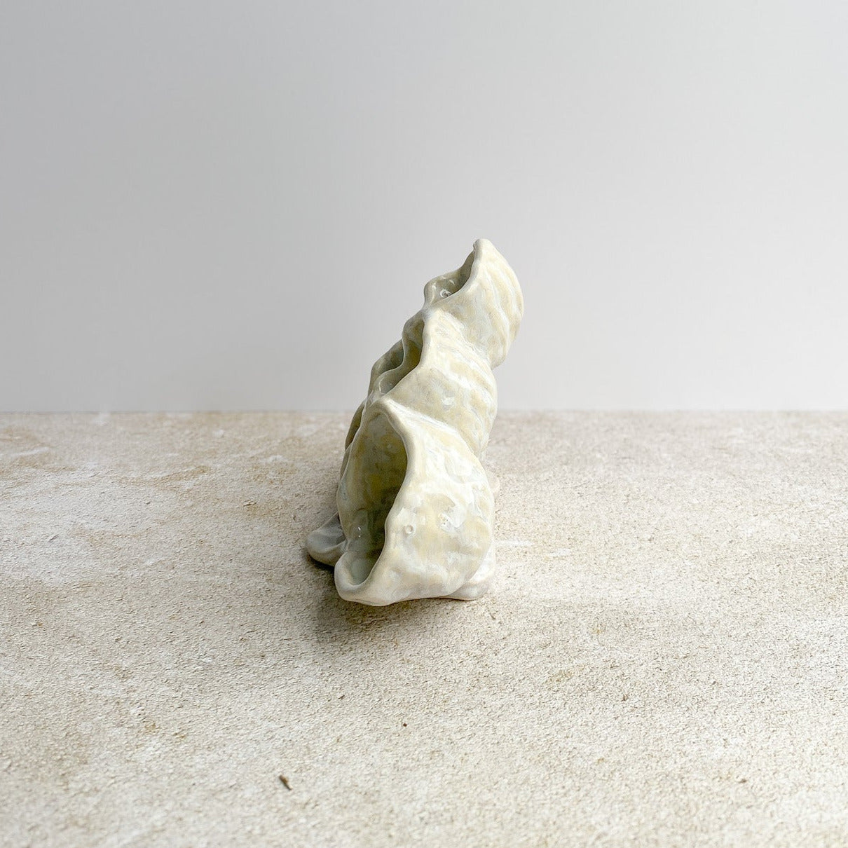 White ceramic sculpture on a textured surface with a light gray background