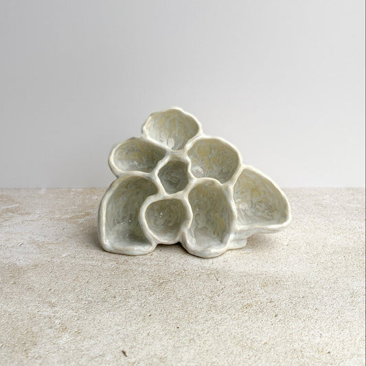 Ceramic sculpture with an organic form on a textured surface with a plain background