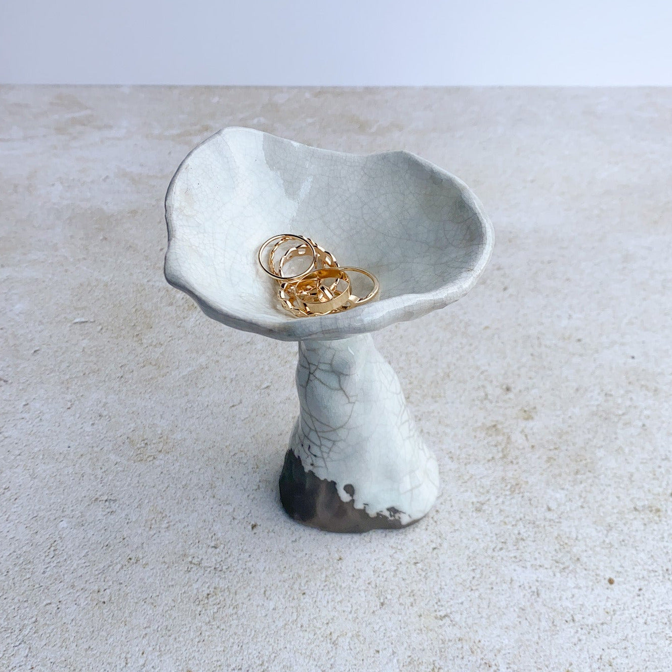 Ceramic ring holder with gold rings on a textured surface