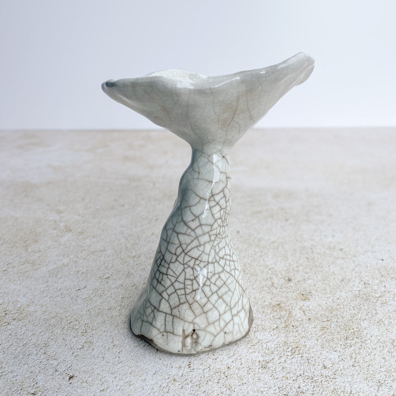 Ceramic mushroom sculpture on a textured surface with a light gray background