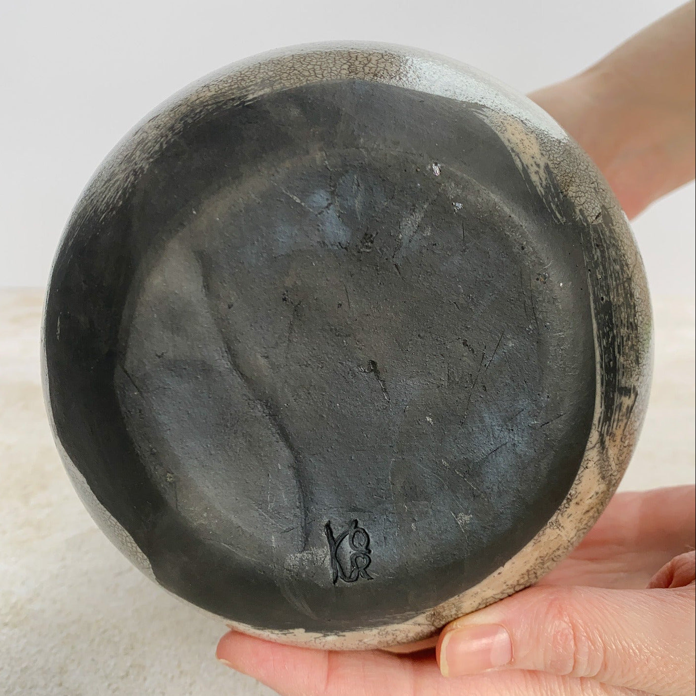 Hands displaying bottom of a raku ceramic vase on a light background