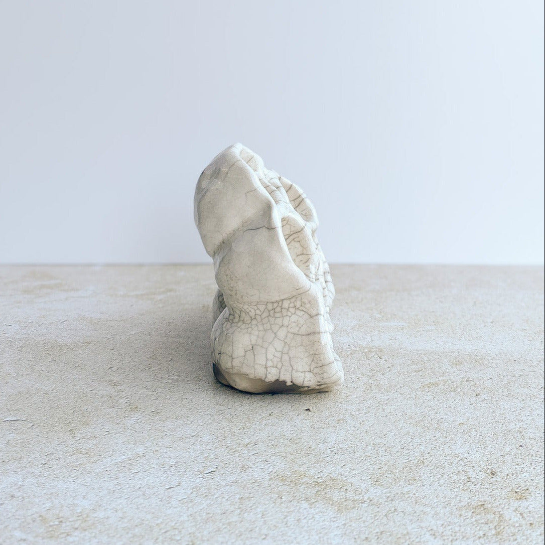 White ceramic sculpture on a light surface with a white background
