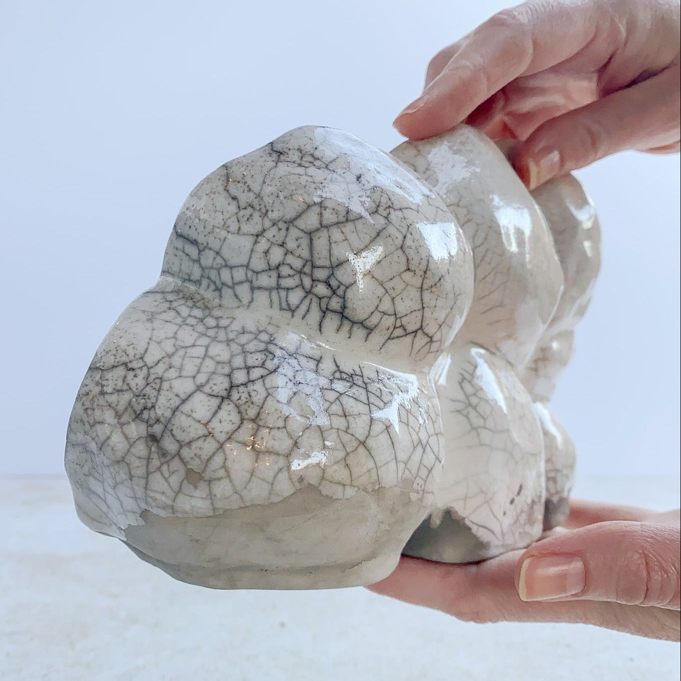 Ceramic object with a raku crackle glaze held by hands against a light background