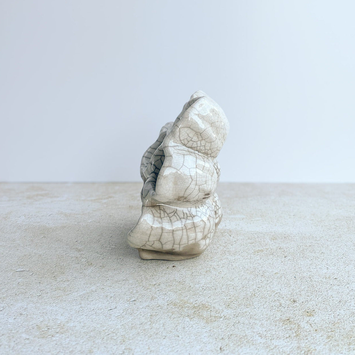 White ceramic sculpture on a textured surface with a light gray background