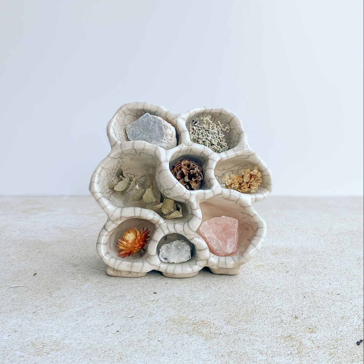 Ceramic holder with small compartments filled with decorative items on a white surface.