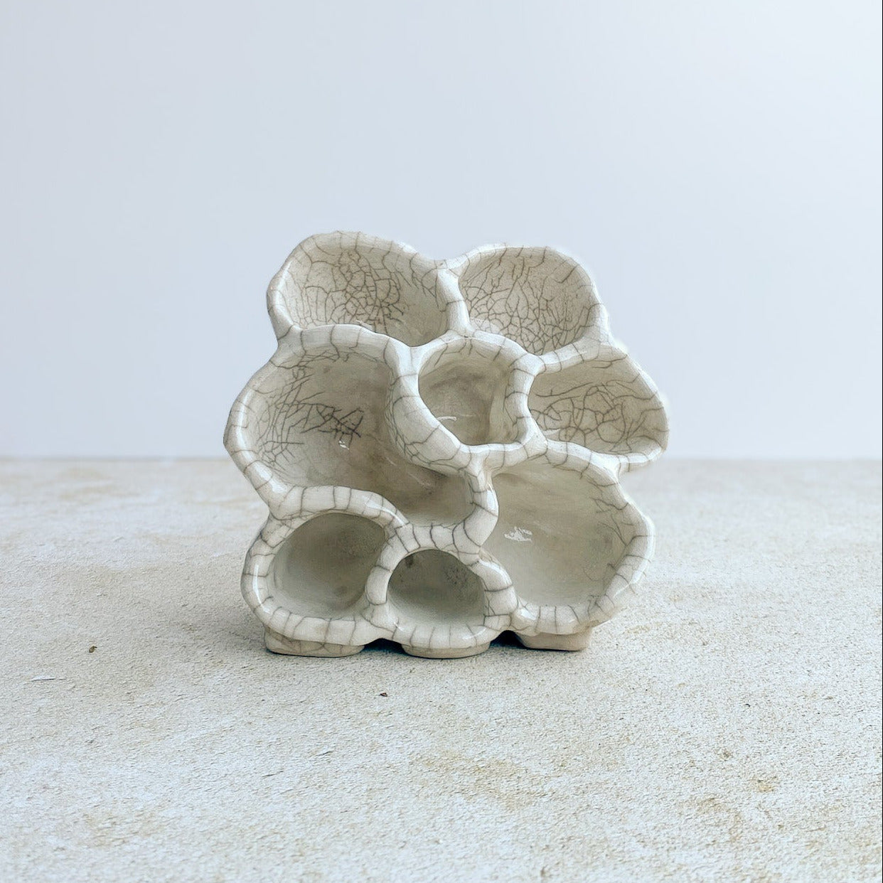 Ceramic organic sculpture vessel on a textured surface with a white background