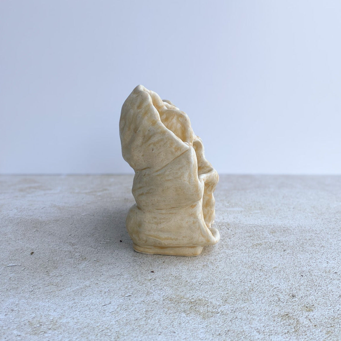 Small beige ceramic sculpture on a textured surface with a light gray background